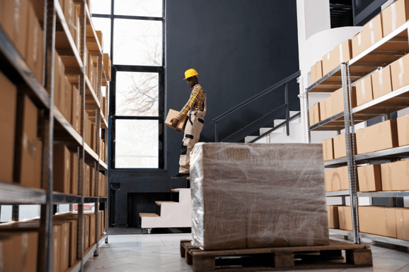 Un trabajador casco bajando escaleras en un almacén, llevando una caja para la tarima de madera